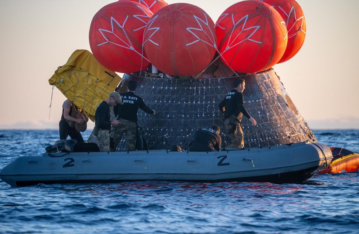 U.S. Navy personnel on an inflatable raft beside the floating Orion capsule, which is topped by red uprighting bags