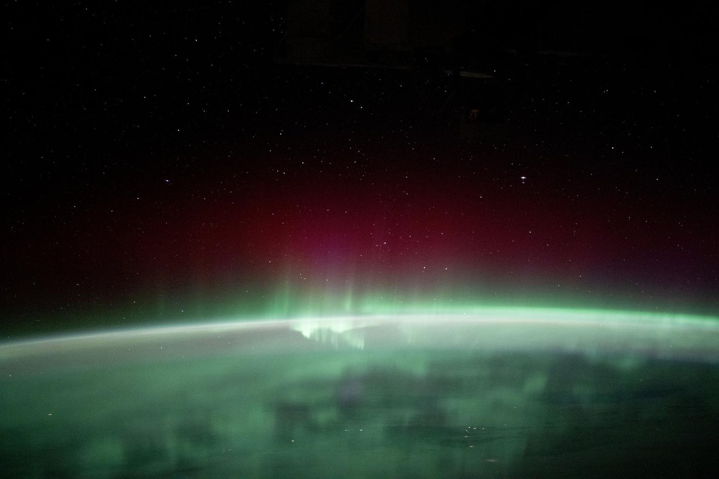 Green and red aurora glowing above Earth's curved horizon, seen from orbit at night