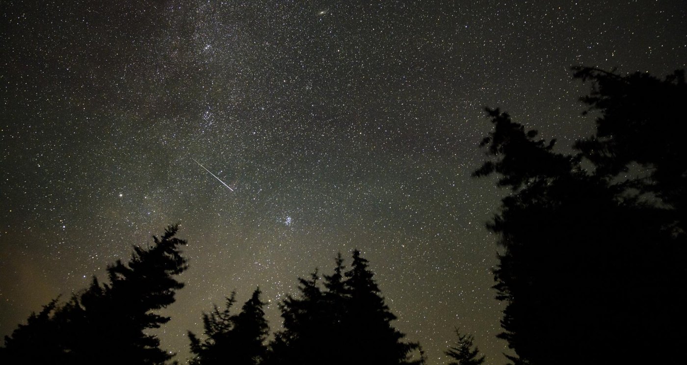 A meteor streaks across a starry night sky over a dark ridge