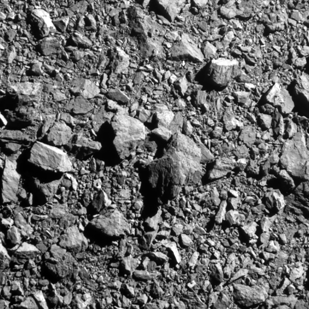 Black-and-white close-up of a rocky asteroid surface covered in boulders, filling the frame