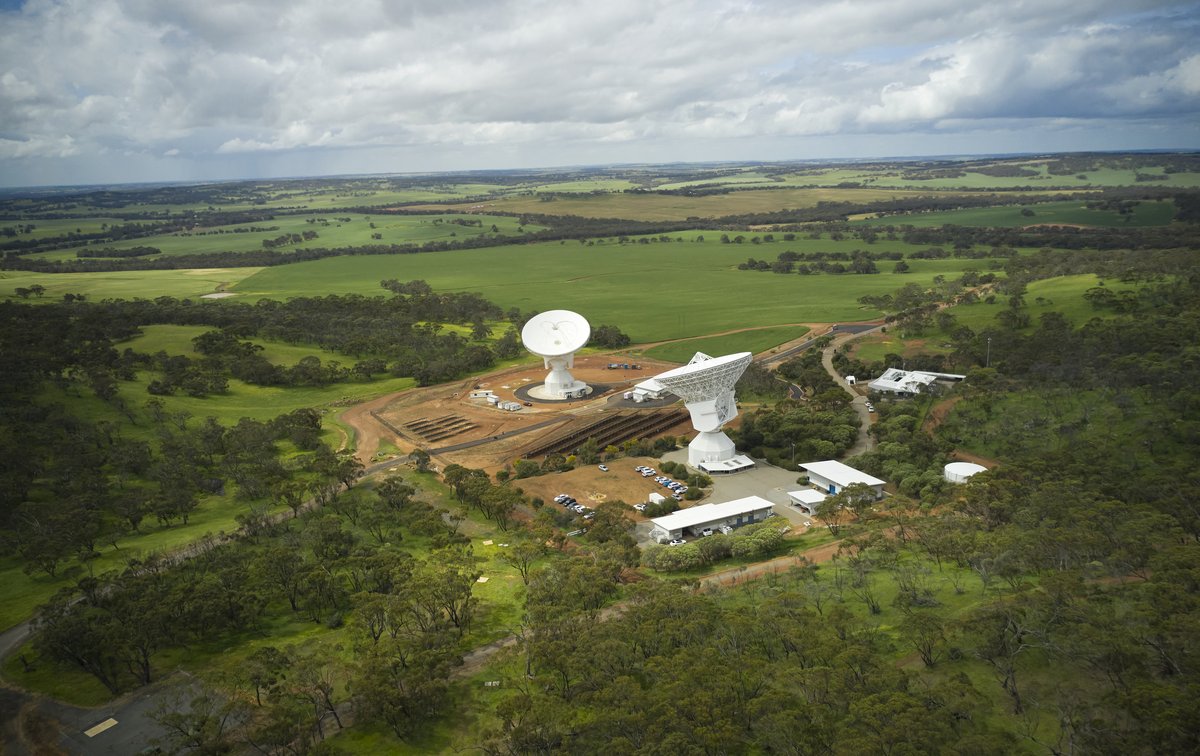 Two large white dish antennas stand on red earth under a blue sky at ESA’s New Norcia ground station in Australia