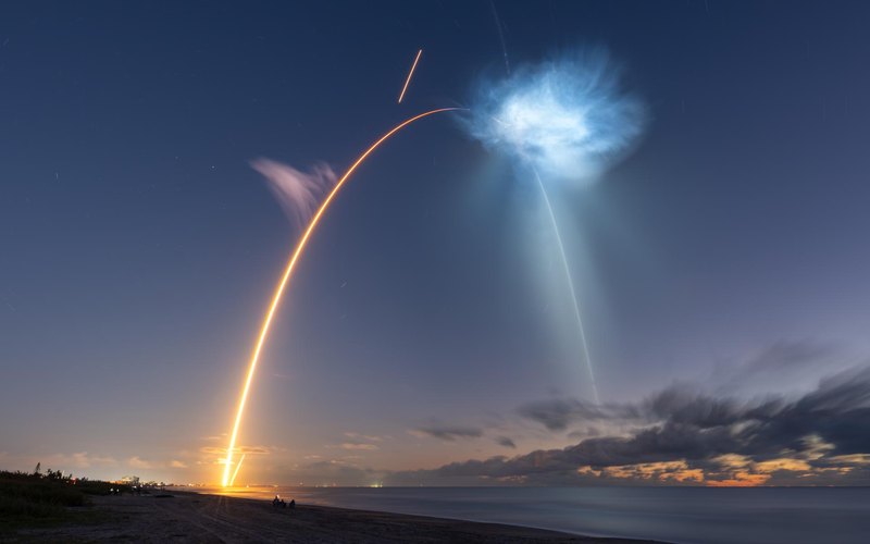 Long-exposure photo of the CRS-35 Falcon 9 launch arc and booster return seen from Cocoa Beach, Oct. 13, 2026 — NASA/John Kraus