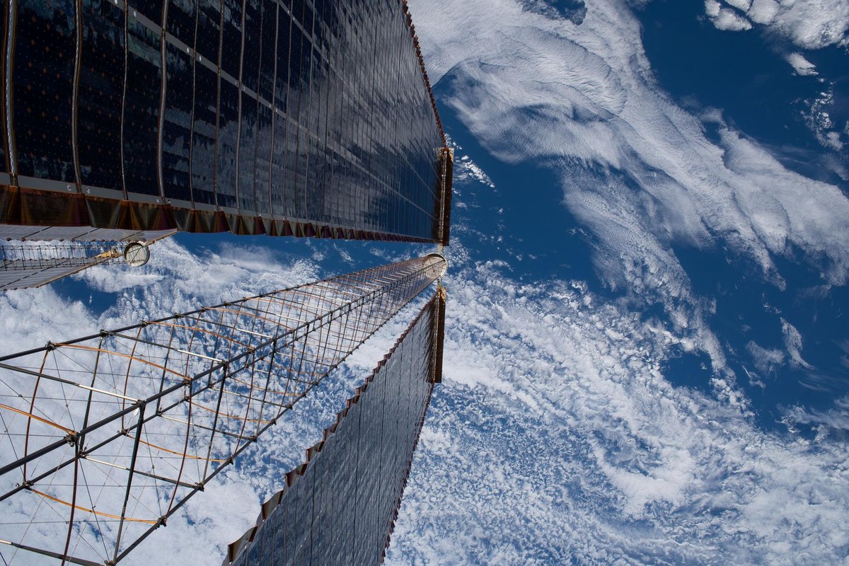 Looking down the length of a pair of the space station’s solar arrays, with blue Earth and white clouds below