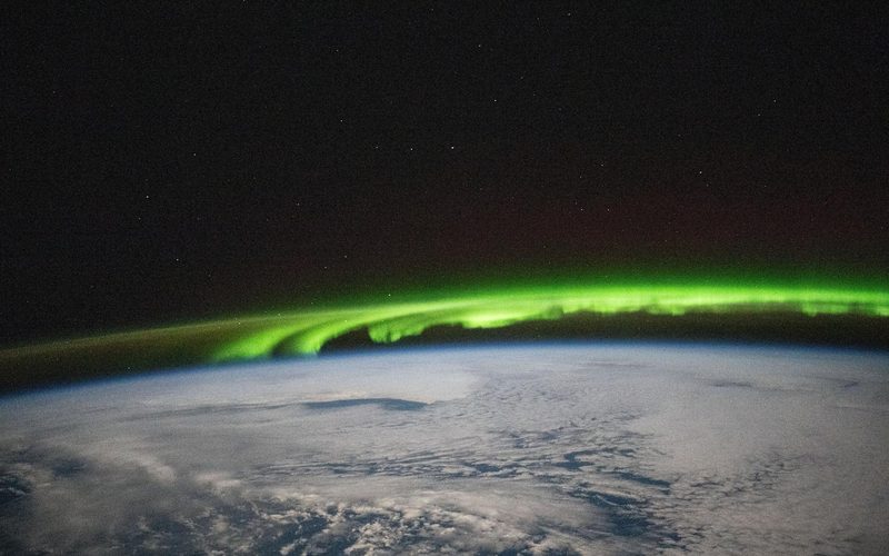 Green aurora borealis above a cloudy North Pacific, seen from the International Space Station — NASA