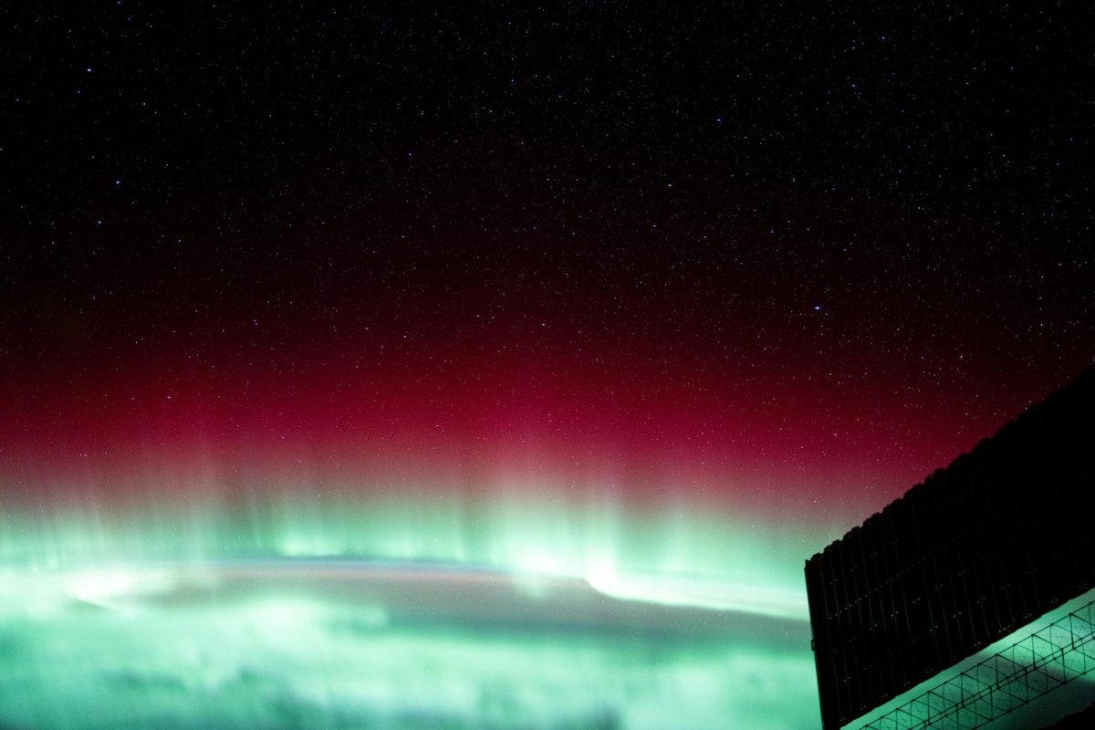 A red and green aurora glows above Earth’s curved horizon, seen from orbit at night