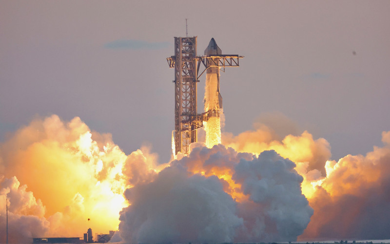 SpaceX Starship lifting off from Starbase next to the launch tower, engines glowing through smoke