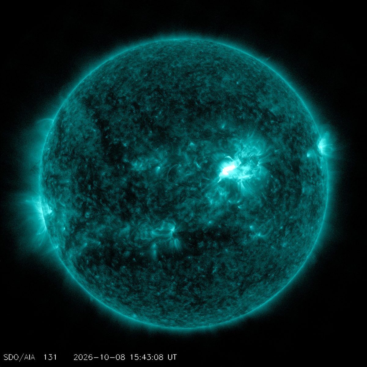 Full disk of the Sun in teal extreme-ultraviolet light, with a bright flare just right of and above center, Oct. 8, 2026, 15:43:08 UTC