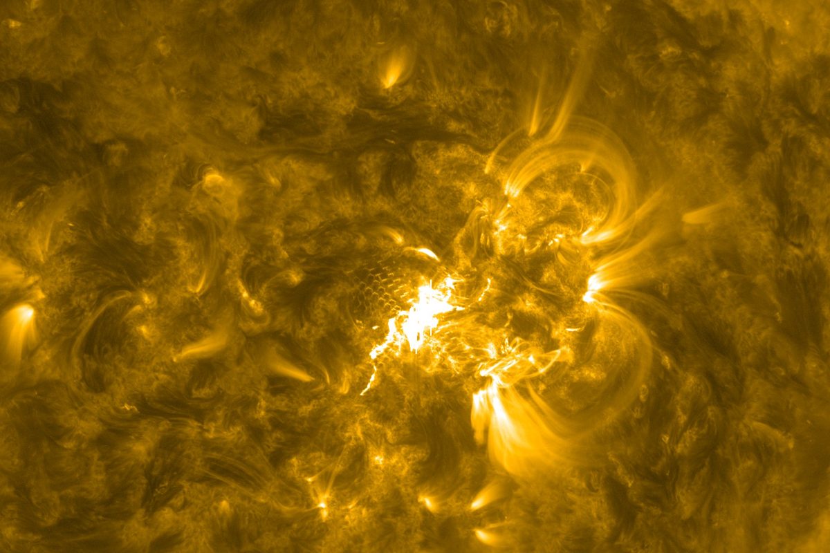 Golden extreme-ultraviolet close-up of the Sun showing bright arching magnetic loops around a white-hot flare site in sunspot Region 4549