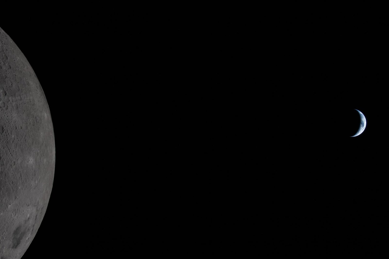 The Moon filling the left side of the frame with Earth as a small crescent in the blackness beyond the lunar limb, photographed by the Artemis II crew
