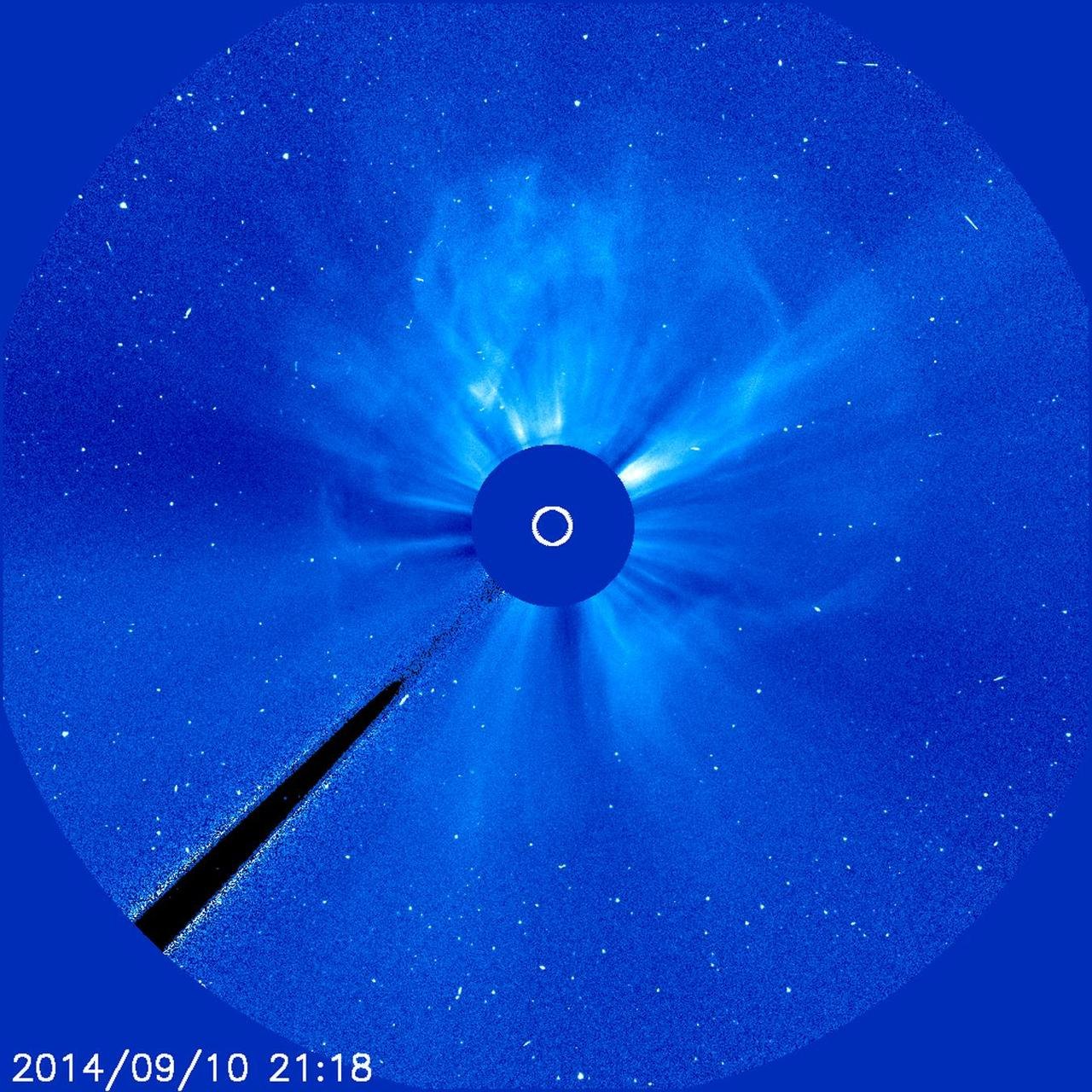 Coronagraph image of a halo coronal mass ejection, a ring of material expanding in all directions around the central disk that blocks the Sun, with bright white specks of energetic particles